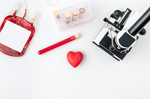 red heart against vials with blood and microscope isolated on white