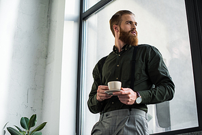 bottom view of businessman standing with cup of coffee and looking at window