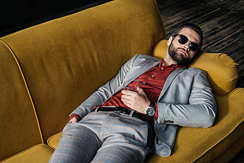 stylish drunk man in sunglasses with glass of cognac lying on yellow sofa