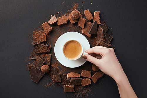 cropped shot of female hand, cup of coffee, truffles and chocolate on grey surface