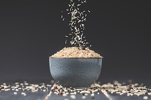 side view of rice spilling into bowl on black table