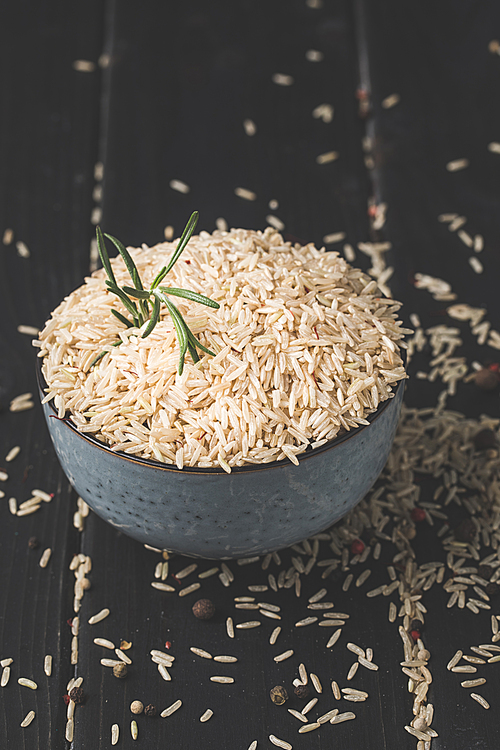 close-up shot of bowl of raw rice with rosemary on black surface