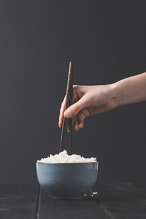 cropped shot of woman taking rice from bowl with chopsticks