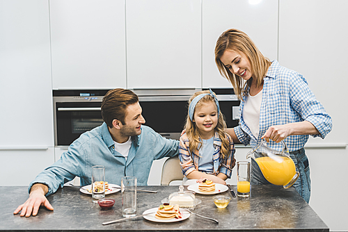 portrait of woman pouring juice into glass during breakfast with family at home