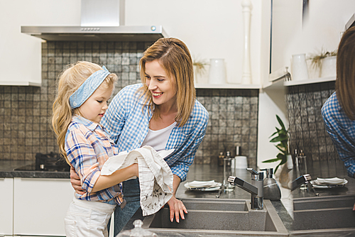 portrait of smiling mother hugging daughter while washing dishes after dinner at home