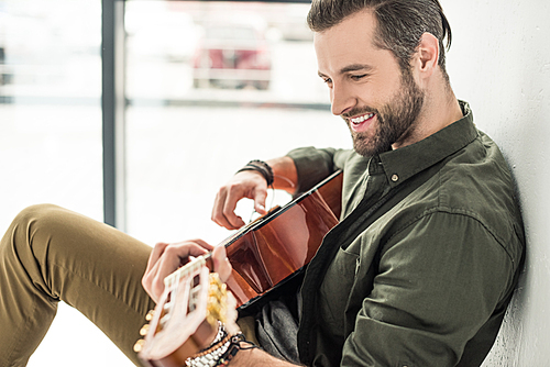 side view of handsome smiling man playing acoustic guitar