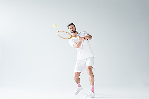 handsome tennis player hitting ball with tennis racket on grey