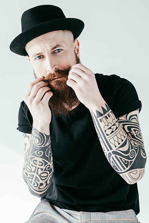 bearded tattooed man twisting mustache and  isolated on white