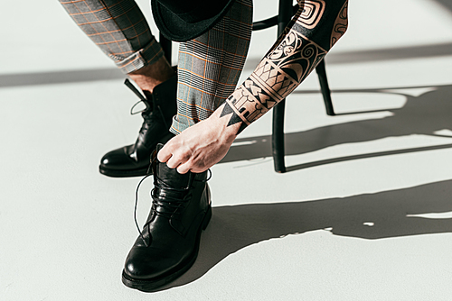 cropped image of tattooed man fixing shoes