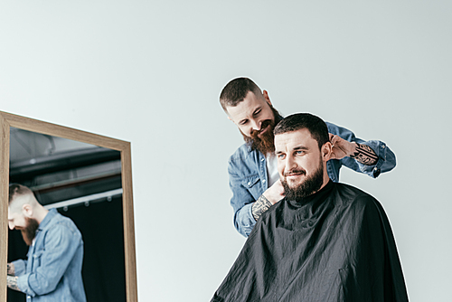 smiling barber shaving customer hair at barbershop isolated on white