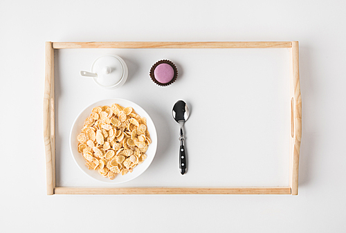 top view of breakfast with cork flakes in bowl and sweet dessert on tray on white surface