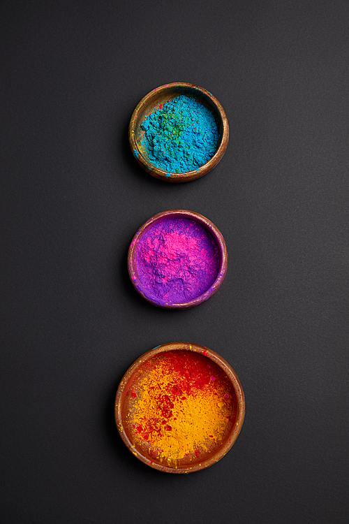 top view of colorful holi paint in bowls in row on grey surface