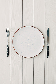 Top view of plate and cutlery on white wooden background