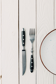top view of empty plate and silverware on white wooden background