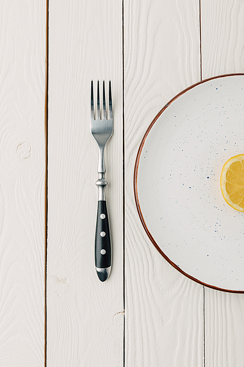 Half of juicy lemon on plate with fork on white wooden background