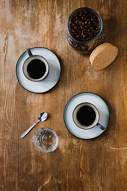 Two cups of black coffee and coffee beans in jar on wooden table