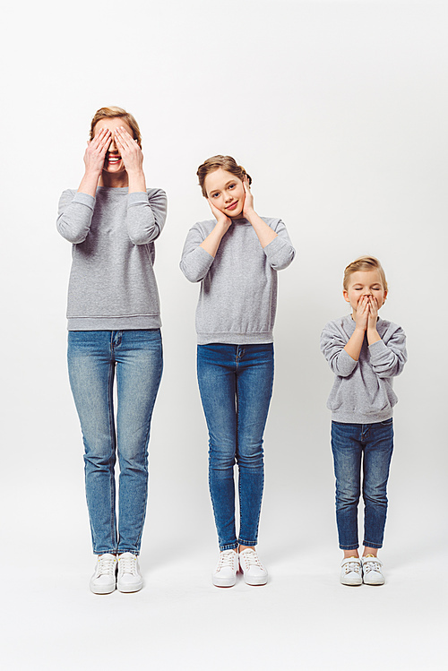 mother and daughters of different generations in similar clothing covering parts of faces isolated on grey