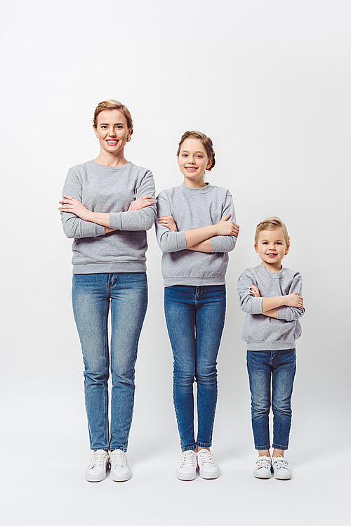 smiling mother and daughters of different generations in similar clothing with arms crossed isolated on grey