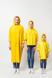 happy mother and daughters in yellow raincoats standing in row on white