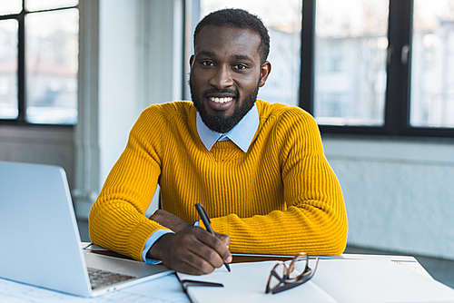 smiling african american businessman holding pen and  in office
