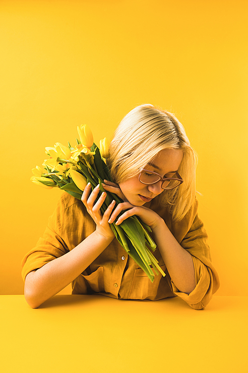 young woman holding beautiful yellow spring flowers on yellow