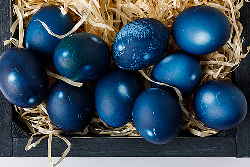 top view of blue painted easter eggs in wooden box with decorative hay