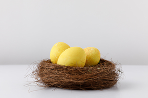 yellow painted easter eggs in decorative nest on white table