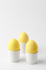 three yellow painted easter eggs in egg stands on white