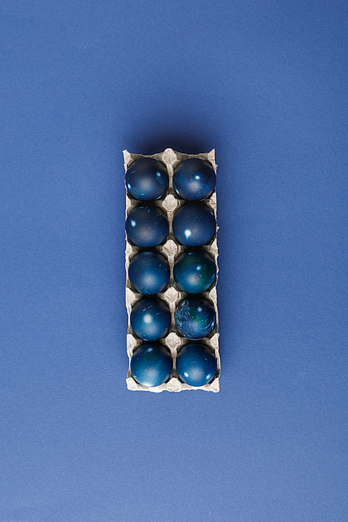top view of blue painted easter eggs in egg tray on blue surface
