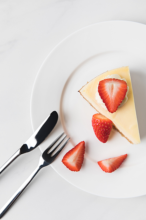 Top view of cheesecake with strawberries and cutlery on white