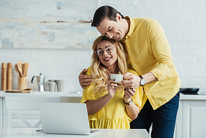 Caring man giving coffee to smiling woman working by laptop