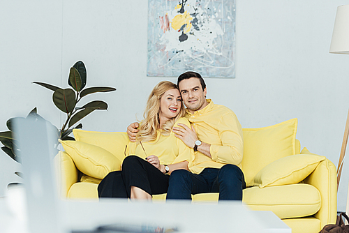 Pretty couple hugging while sitting on yellow sofa