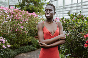 beautiful african american girl with short hair in red dress posing in garden with flowers