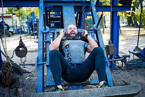 Active man doing exercise for legs on special equipment in outdoor gym