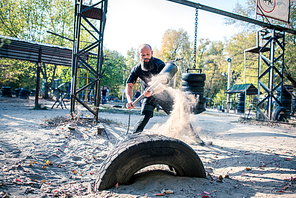 A muscular man hitting a tire with a sledge hammer