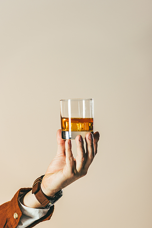 cropped shot of man holding glass of whiskey isolated on beige
