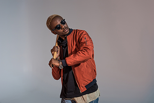 Stylish young african american man holding baseball bat on his shoulder about to kick isolated on light background