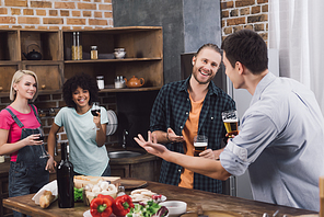 smiling multiethnic friends talking in kitchen with beer and wine