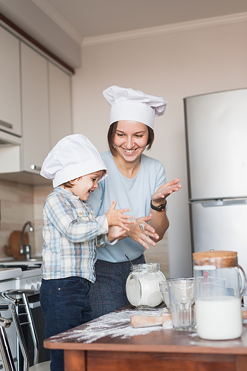 mother and child clapping hands while preparing dough at kitchen