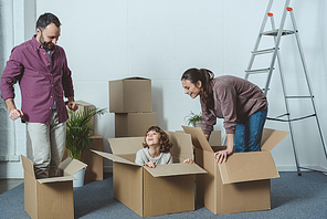 happy parents looking at son sitting in cardboard box during relocation