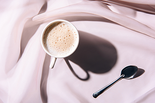 top view of cup of coffee and spoon on pink tablecloth