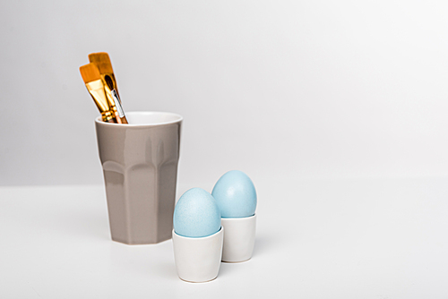 close-up view of blue painted easter eggs and paint brushes in cup on grey
