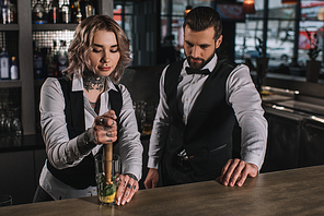 female bartender showing colleague how to prepare drink at bar