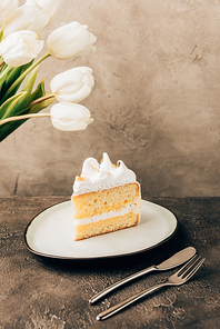 close-up view of delicious piece of cake with whipped cream and beautiful white tulips