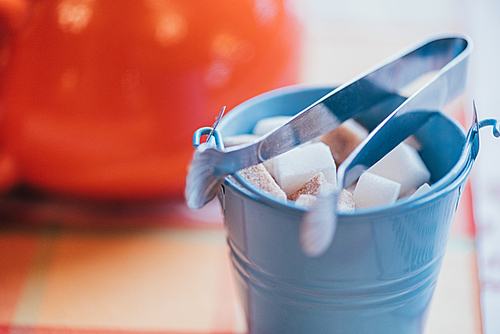 close-up view of small decorative bucket with sugar and tongs on table top