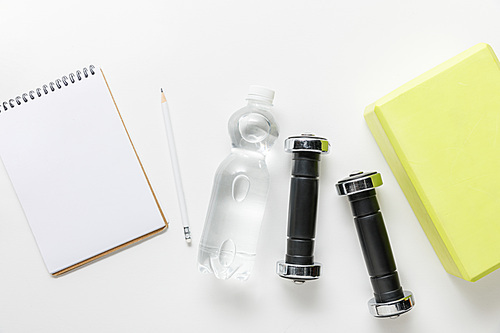 top view of water in bottle, dumbbells and blank notebook with pencil near box on white background