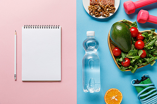 top view of bottle with water, diet food, sport equipment and blank notebook on blue and pink background