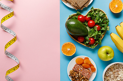 top view of diet food on blue and measuring tape on pink background