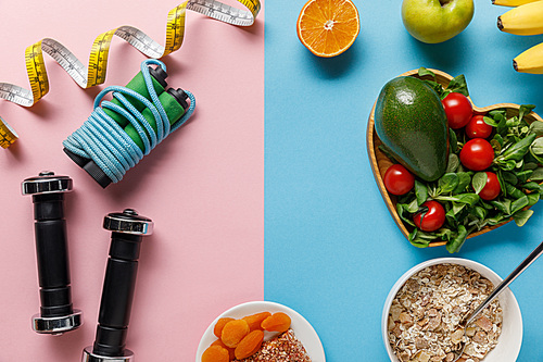top view of delicious diet food and sport equipment with measuring tape on blue and pink background