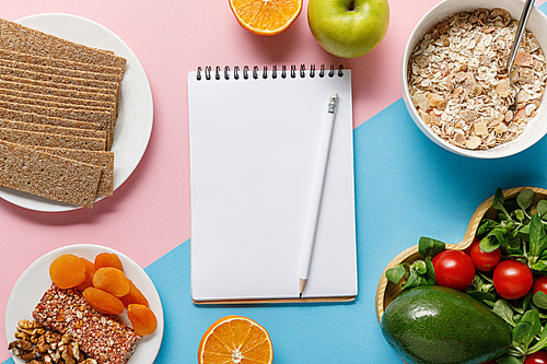 top view of empty notebook and pencil with tasty diet food on blue and pink background